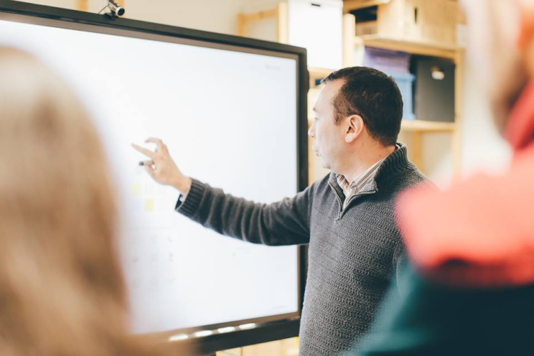 Man pointing at a large interactive whiteboard during a meeting with blurred people in foreground