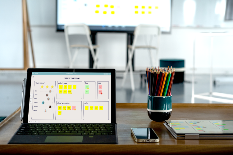 Tablet on a desk displaying a weekly meeting board with sticky notes